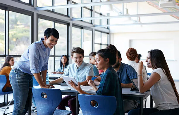 Teacher assisting group of students in classroom, looking at tablet